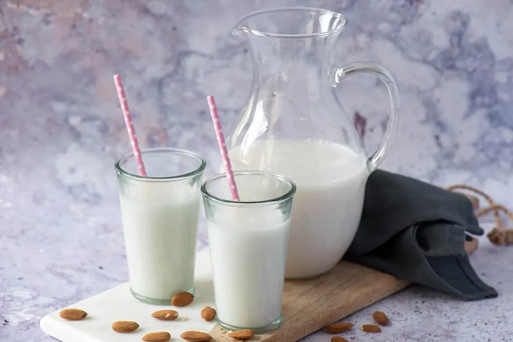 Selbstgemachte Mandelmilch in einer Glasflasche neben eingeweichten Mandeln und Nussmilchbeutel, bereit für die Zubereitung.