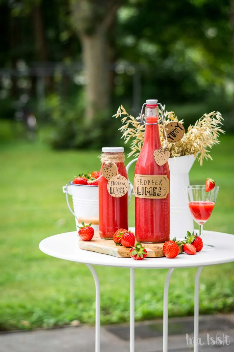 Selbstgemachter Erdbeerlimes in mehreren Flaschen, dekoriert mit frischen Erdbeeren, ideal für Partys und Mädelsabende.
