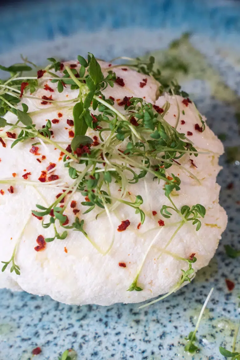 Selbstgemachter Frischkäse mit frischen Kräutern auf einem Holztisch angerichtet.