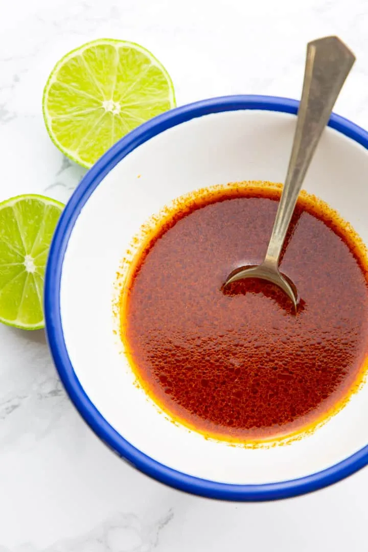 Selbstgemachtes Limetten-Koriander-Dressing für mexikanischen Salat, appetitlich angerichtet in einer weißen Schale auf einer eleganten Marmorplatte, daneben frische Limetten und Koriander.