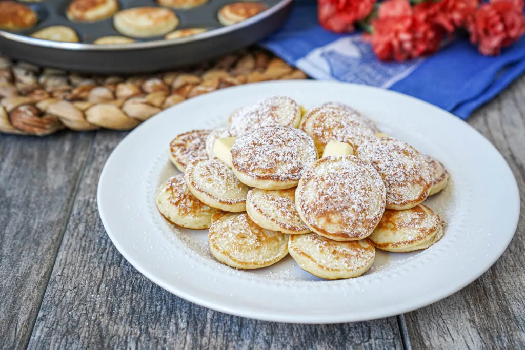 Servierfertige Poffertjes mit Butter und Puderzucker auf einem weißen Teller