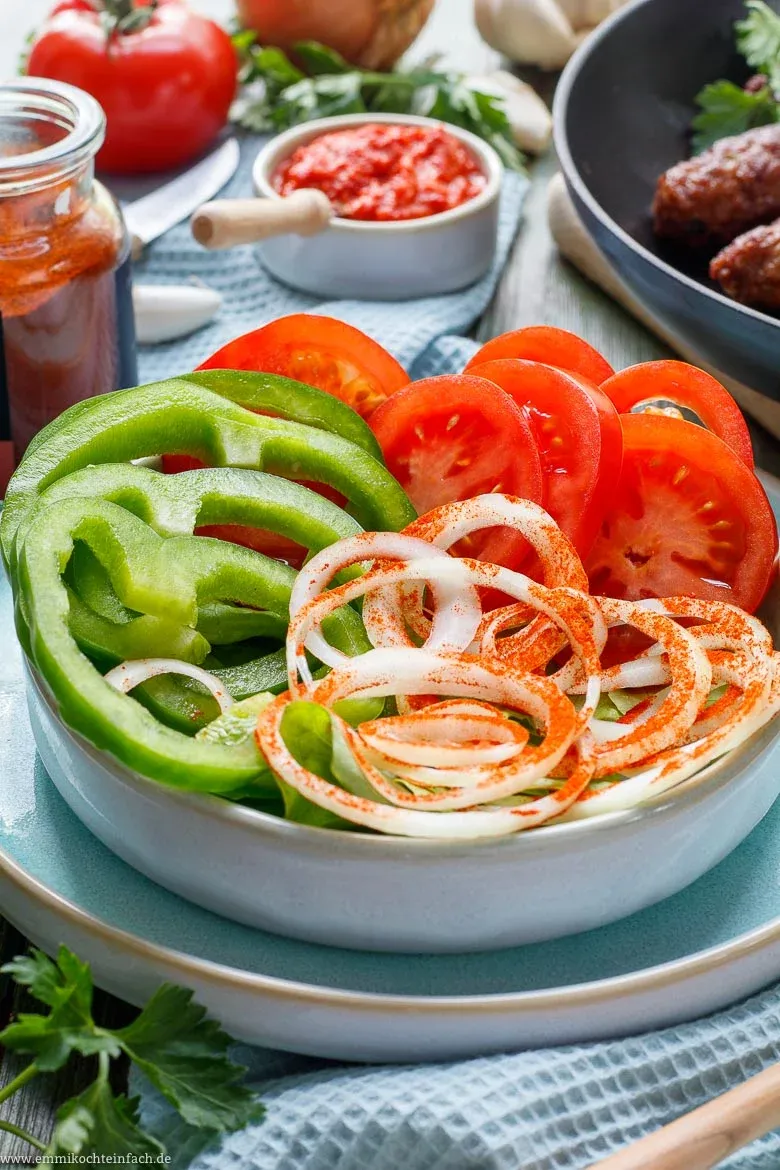 Servierte Cevapcici mit frischer Beilage aus Zwiebeln und Tomaten
