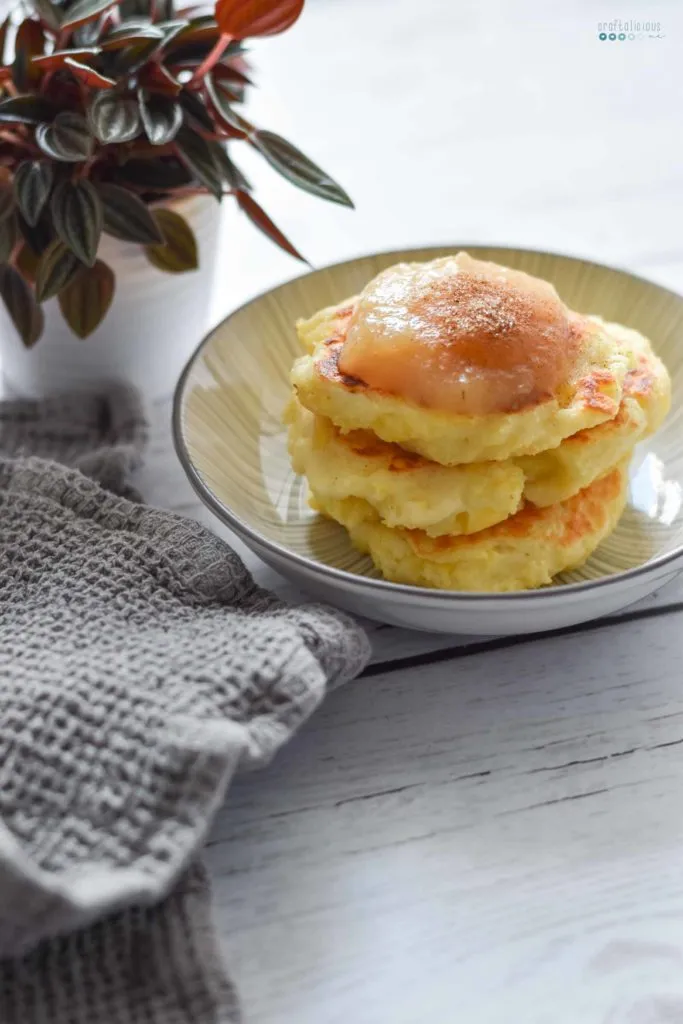 Servierte Sächsische Quarkkeulchen auf einem Teller, liebevoll angerichtet mit süßem Apfelmus und duftendem Zimtzucker.