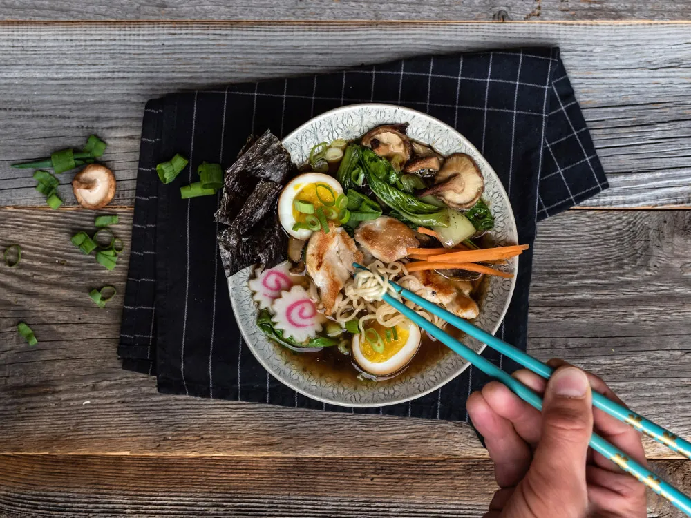 Servierte schnelle Ramen Suppe mit Hähnchenwürfeln, Ei und frischen Kräutern in einer Schale.