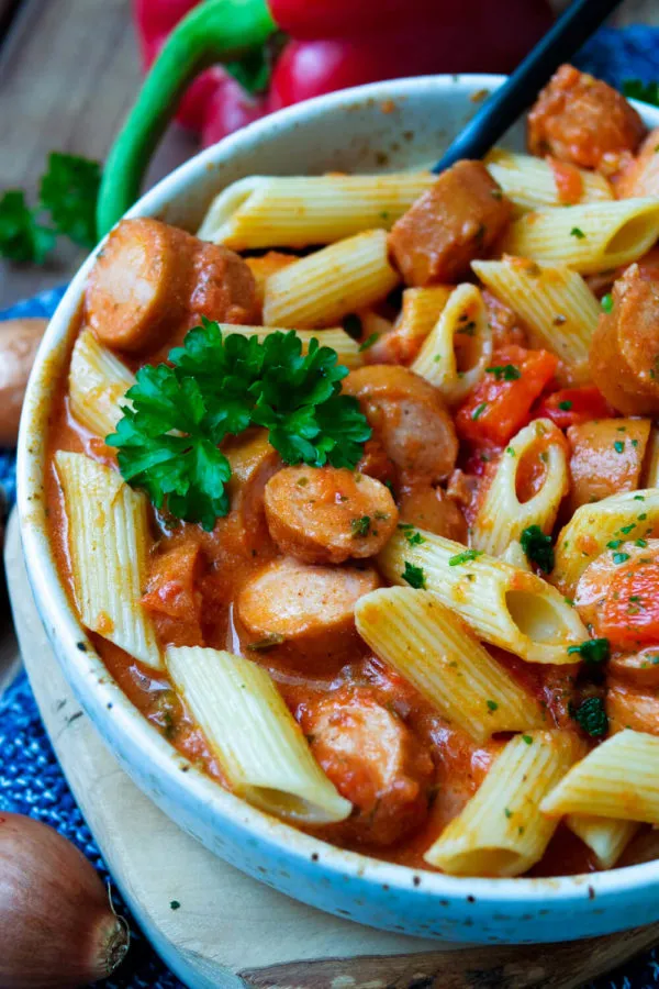 Serviertes Würstchengulasch mit Tomatensauce und Nudeln in einer rustikalen Schale