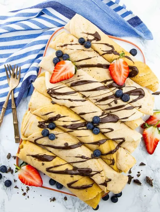 Sieben fluffige vegane Pfannkuchen auf weißem Teller mit frischen Erdbeeren und Schokoladensauce auf Marmoroberfläche