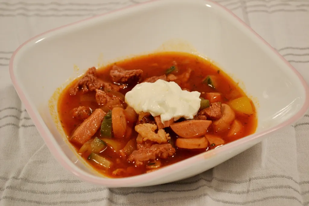 Soljanka mit Fleisch, Wurst, Gurken und Paprika in einer Schale serviert.