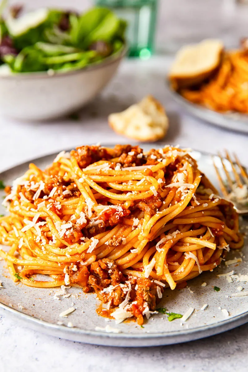 Spaghetti Bolognese auf grauem Teller mit frischem Salat