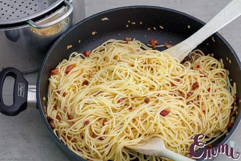 Spaghetti werden in der Pfanne mit Speck vermengt