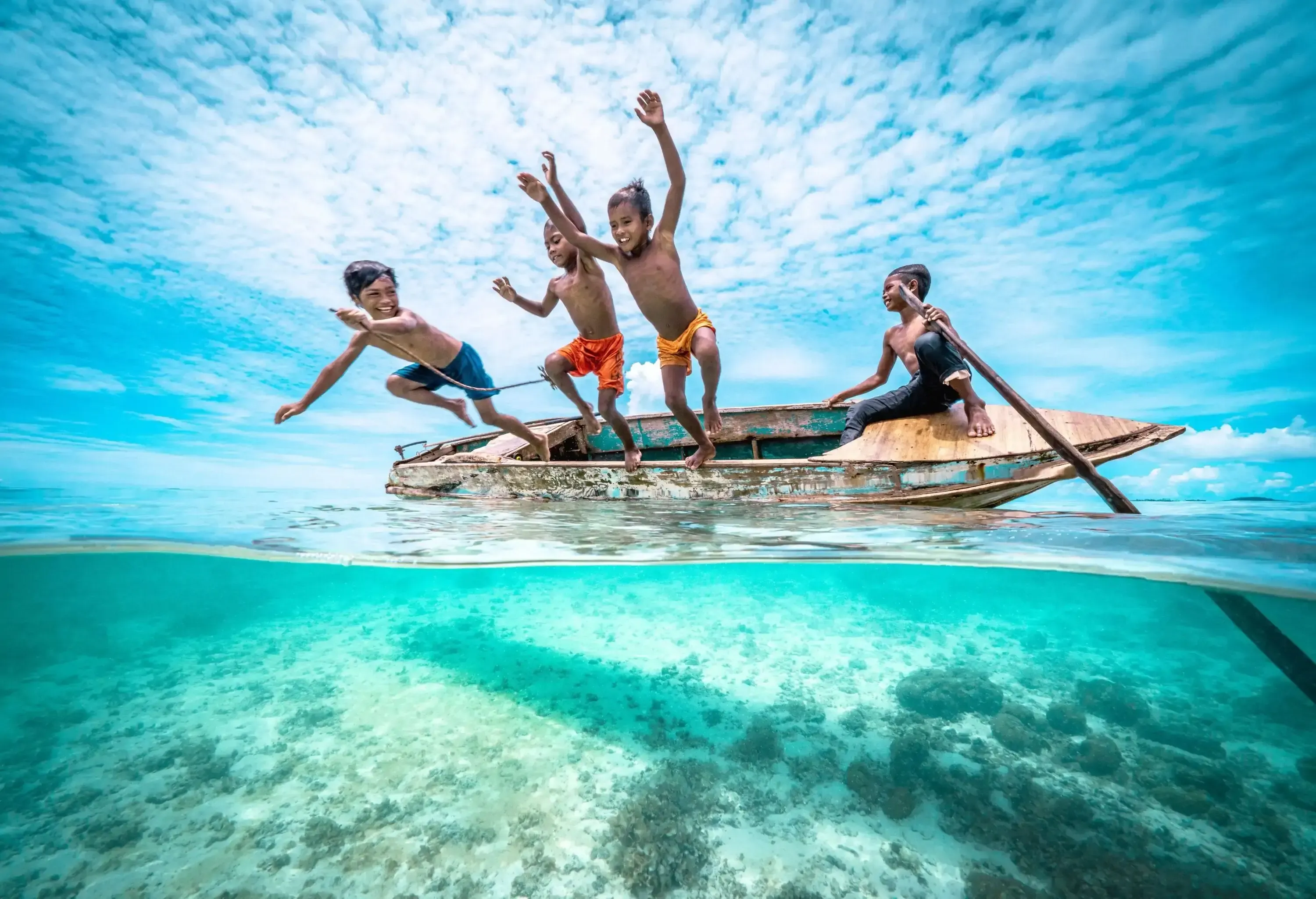 Split wide angle shot of Bajau Children Jumping off wooden canoe and dive into the ocean of a tropical island beach.
