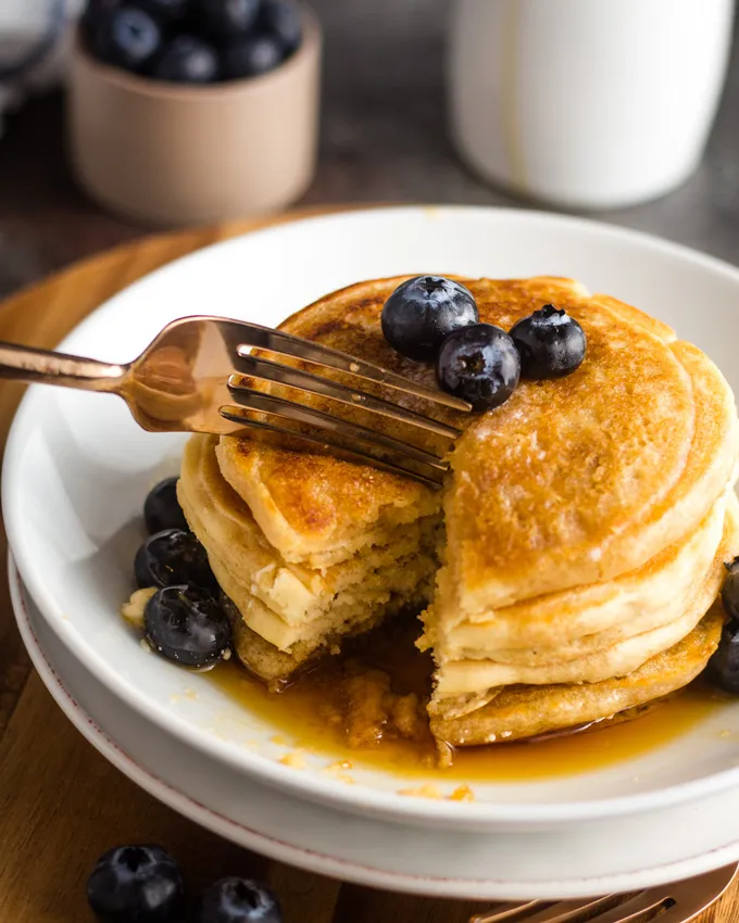 Stapel Pancakes auf weißem Teller mit goldener Gabel