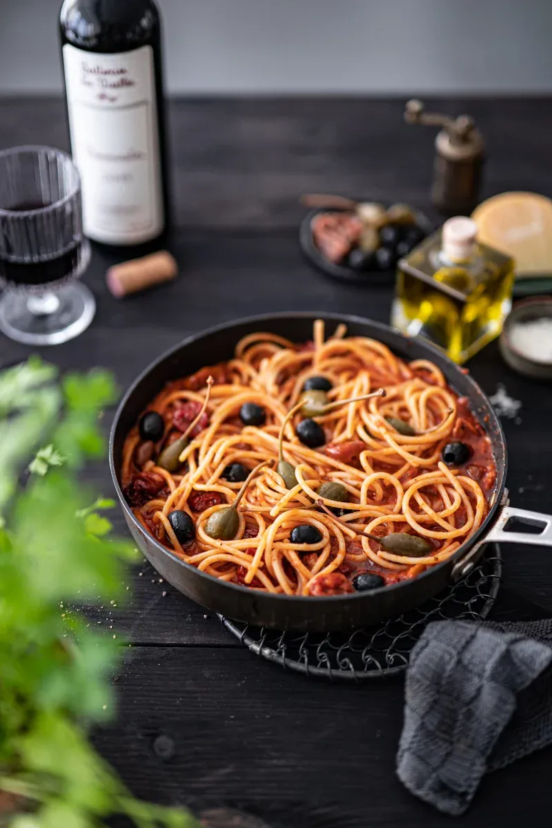 Teller mit Spaghetti alla Puttanesca und frischem Basilikum