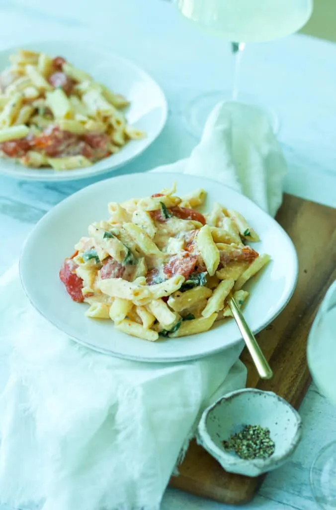 Teller Tomaten-Feta-Pasta mit goldener Gabel und Weinglas