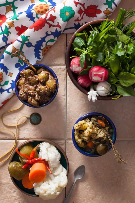 Tischplatte mit einer Auswahl an frischen Kräutern, eingelegten Oliven und Mixed Pickles