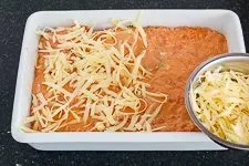 Tomaten-Sahnesoße über die gefüllten Cannelloni gießen und mit geriebenem Käse bestreuen
