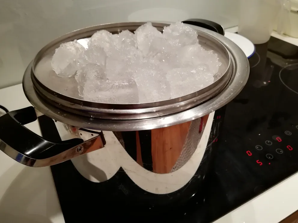 Topf mit umgedrehtem Deckel, der mit Eis für die Destillation von alkoholfreiem Gin bedeckt ist