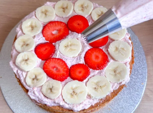 Tortencreme wird aus dem Spritzbeutel auf die Fruchtschicht der Geburtstagstorte aufgetragen