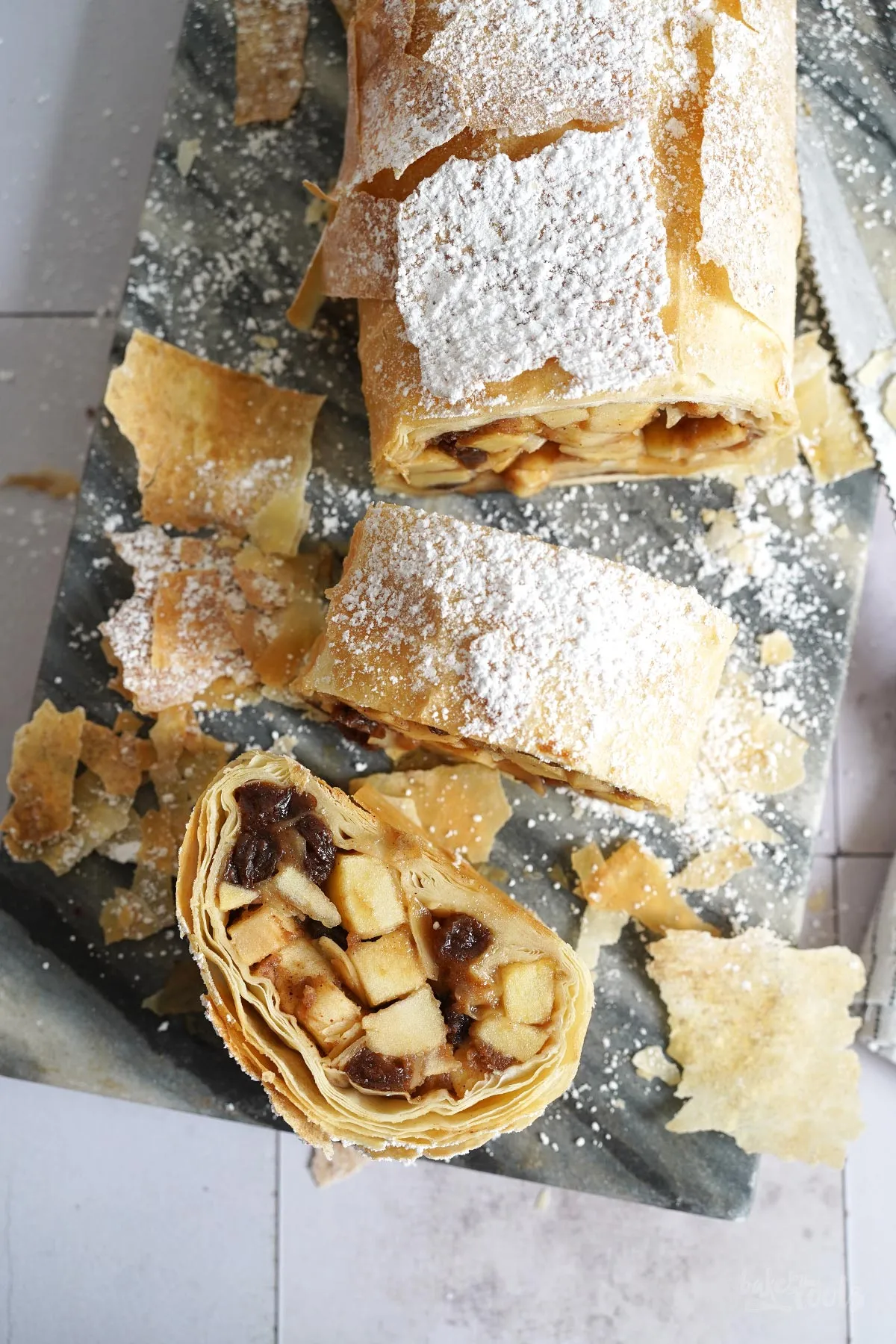 Ungebackener Apfelstrudel aus Filoteig auf Backpapier, bereit zum Backen, zeigt die Schichten des Teigs und die Apfelfüllung.
