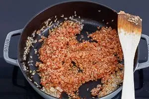 Ungekochter Paella-Reis wird mit passierten Tomaten vermengt