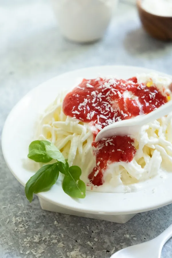 Vanilleeis als Spaghettieis auf einem Teller mit Erdbeersauce und weißer Schokolade