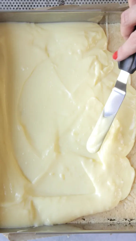 Vanillepuddingcreme wird auf den vorbereiteten Kuchenboden aufgetragen