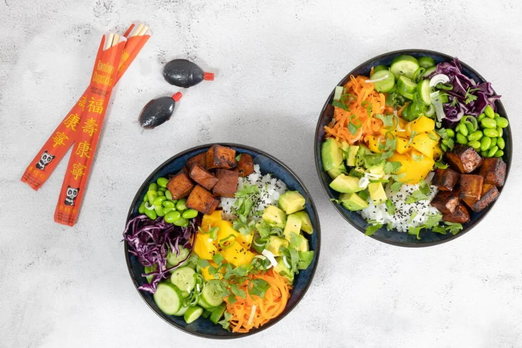 Vegane Poke Bowl mit Tofu, Sojasauce und Essstäbchen auf Holztisch