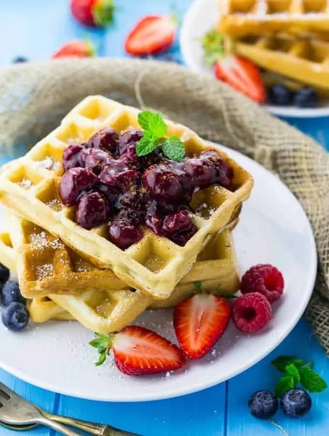 Vegane Waffeln mit Kirschsauce auf weißem Teller, garniert auf blauem Holzgrund