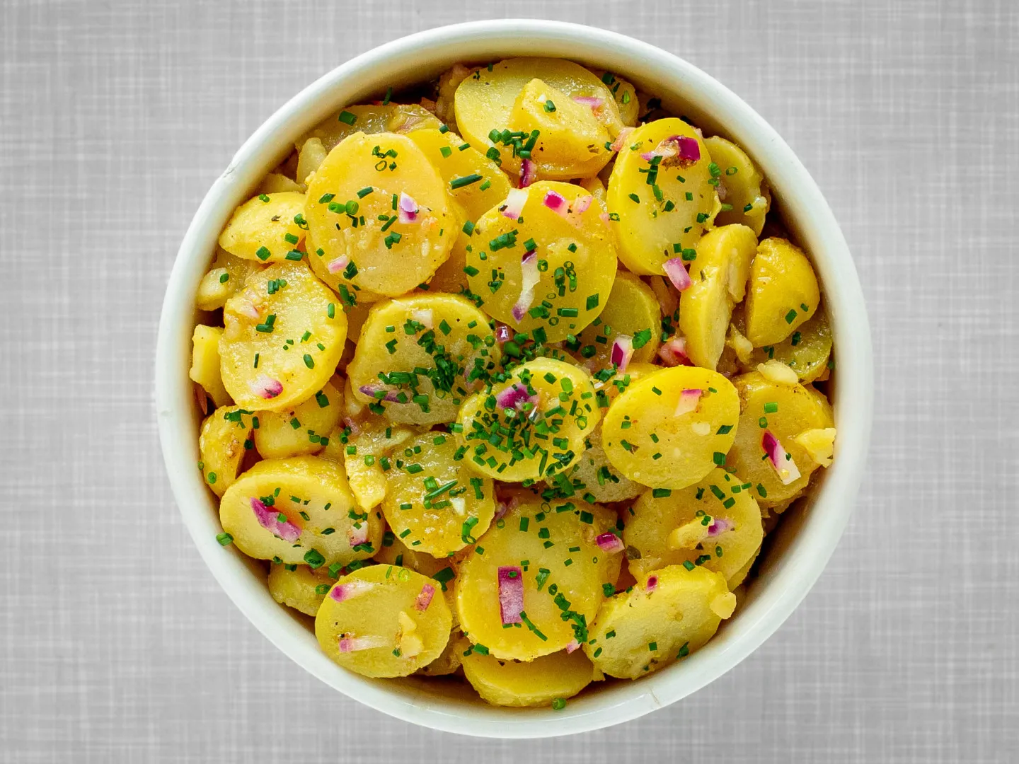 Veganer Kartoffelsalat nach Wiener Art, in einer Schüssel angerichtet und mit frischem Schnittlauch garniert, von oben fotografiert.