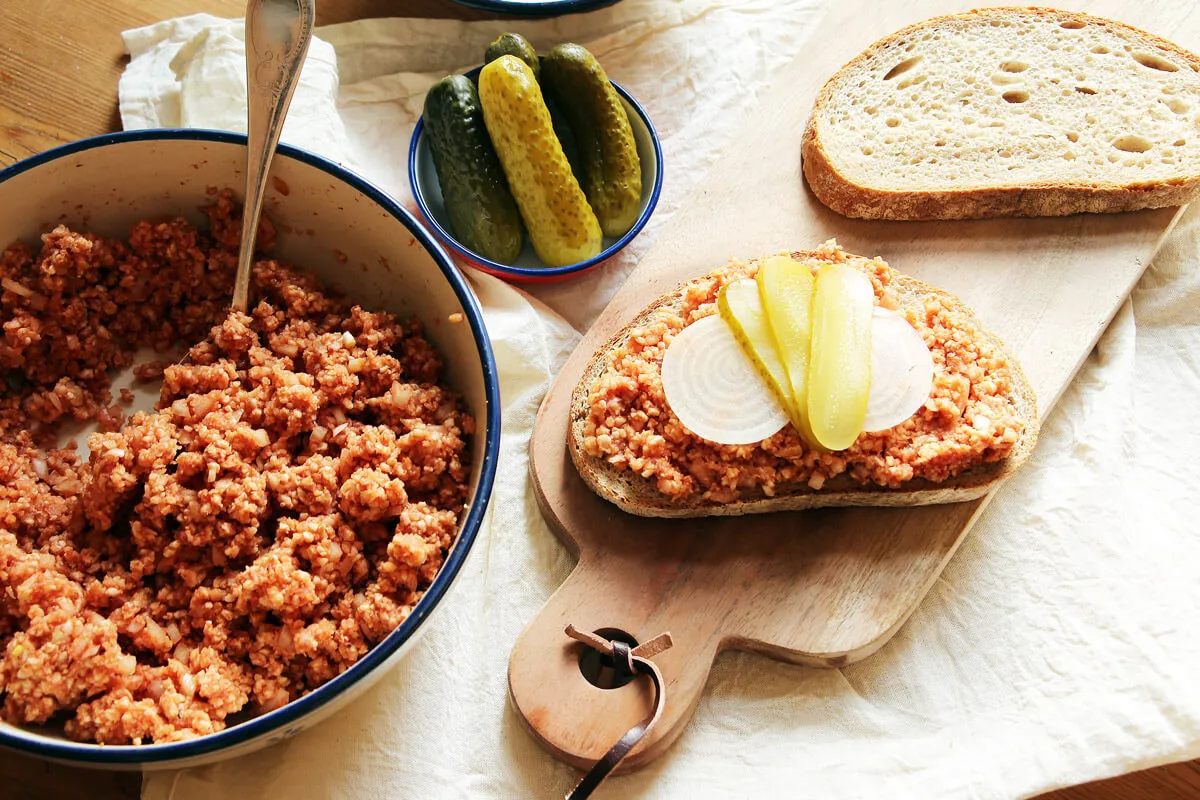 Veganes Mett auf frischem Brötchen, garniert mit Zwiebeln und Gurken