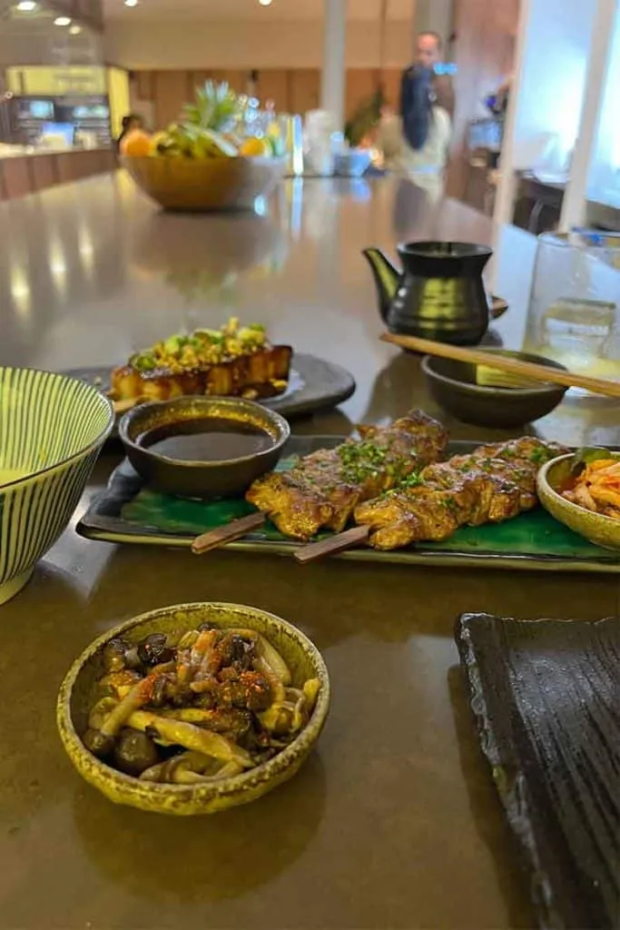 Verschiedene Gerichte im Kiyomi, einem gehobenen asiatischen Fusionsrestaurant in Zagreb, darunter sautierte Pilze und gegrillte Fleischspieße mit Kimchi, serviert auf einem ansprechenden Tisch.