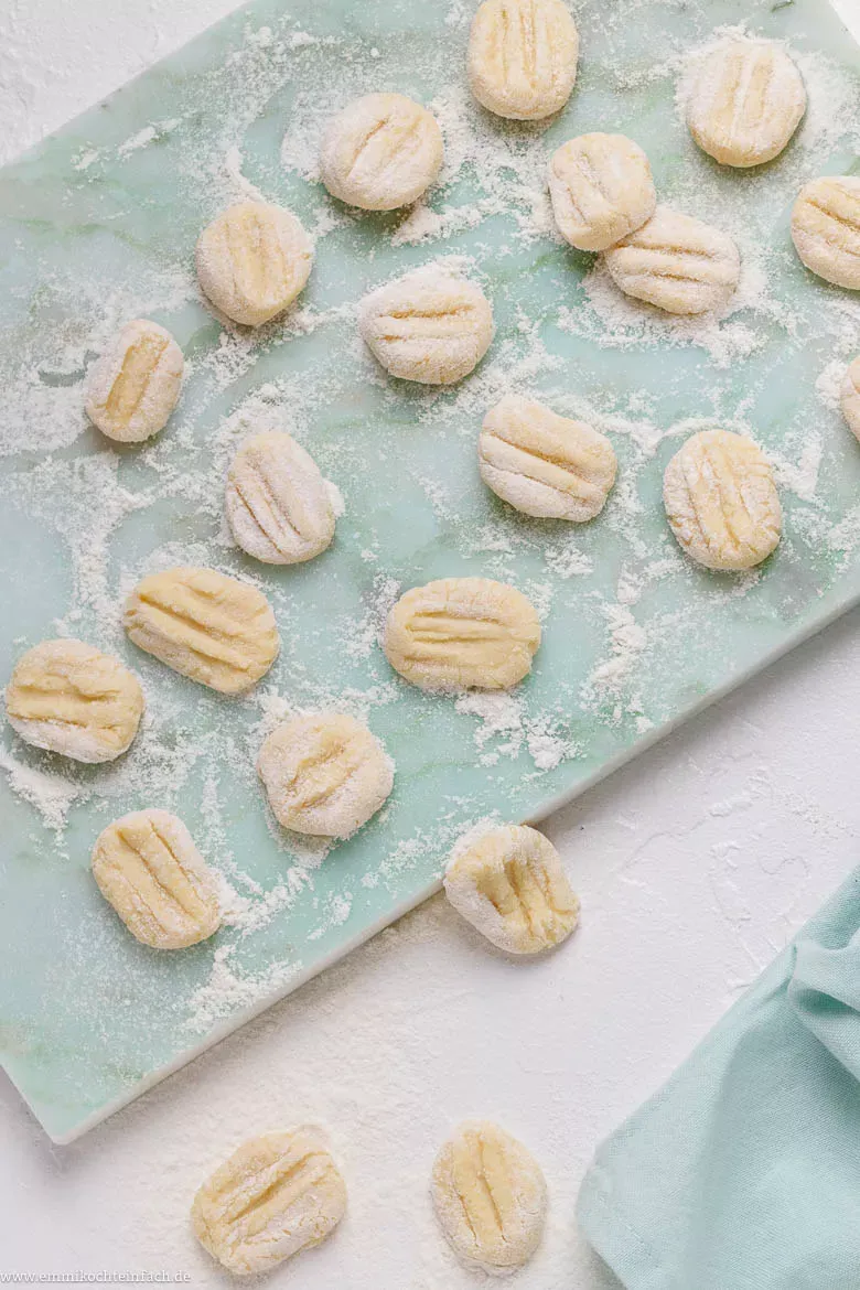 Verschiedene Zutaten für Gnocchi auf einem Holztisch arrangiert: Mehlig kochende Kartoffeln, Weizenmehl, Hartweizengrieß und eine Prise Salz. Die Komposition betont die Einfachheit der Zutaten und lädt zum Selbermachen ein. Alternative-Text optimiert für das Keyword &quot;Gnocchi selber machen&quot; und relevante Suchbegriffe.