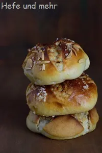 Vier Campingwecken, zwei davon gefüllt mit Hagelzucker und zwei mit Mandelstückchen, auf einem Holztisch, zeigen regionale Backtradition.