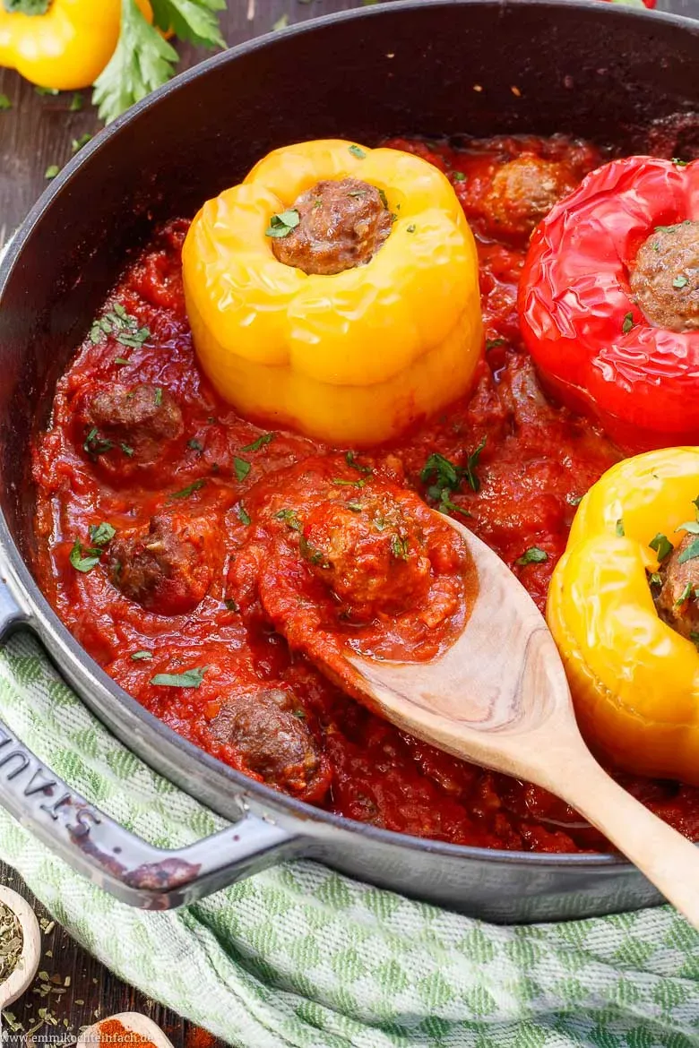 Vier goldbraun gebackene gefüllte Paprikaschoten mit Hackfleisch in einem Topf mit reichlich Tomatensoße