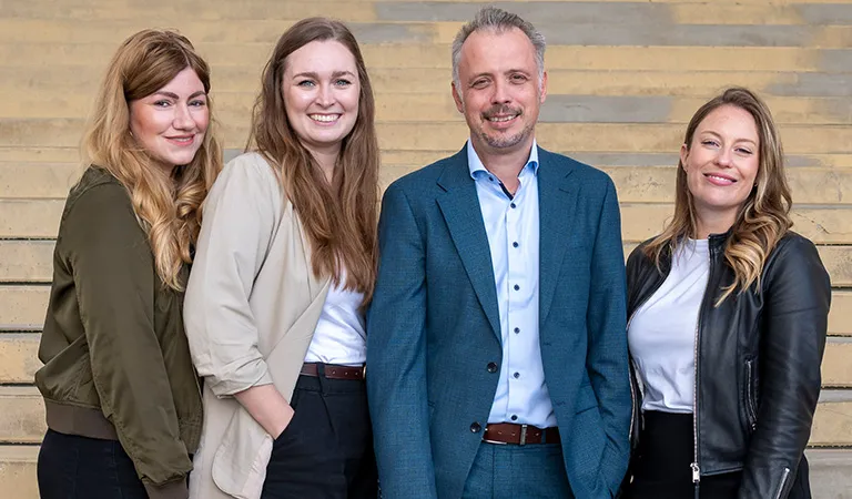 Vier Personen lächeln vor Treppen, lockere und formelle Kleidung in Erdtönen