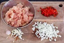 Vorbereitungsschritt: Geschnittenes Hähnchenbrustfilet, gewürfelte Zwiebeln, Knoblauch und Peperoni bereit zum Anbraten für den Erdnuss-Hähnchen-Topf, ein Element vieler afrikanischer Rezepte.