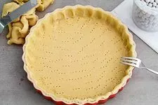 Vorgebackener Mürbeteig in einer roten Quicheform