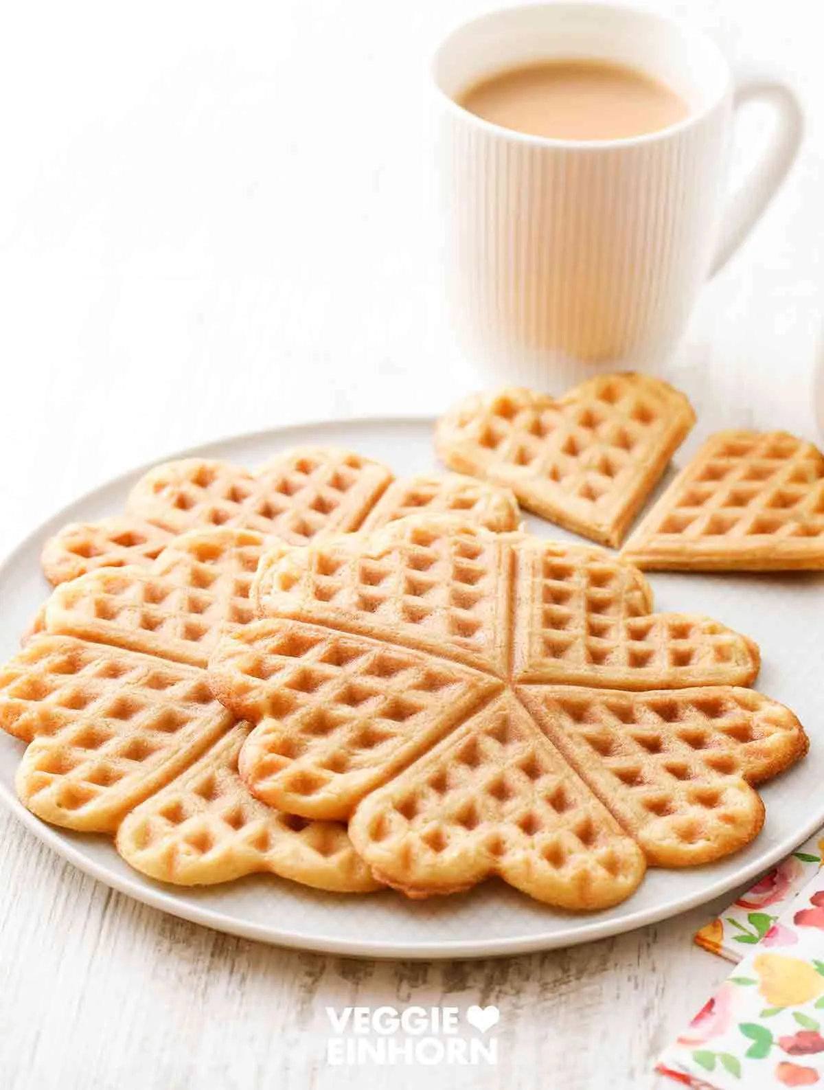 Waffeln ohne Ei serviert auf einem rustikalen Teller, daneben eine Tasse mit cremigem Milchkaffee, perfekt für eine deutsche Kaffeetafel.