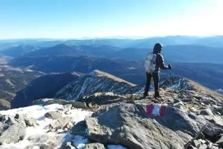 Wanderin mit Daunenjacke auf einem Grat, Blick auf schneefreie Berge