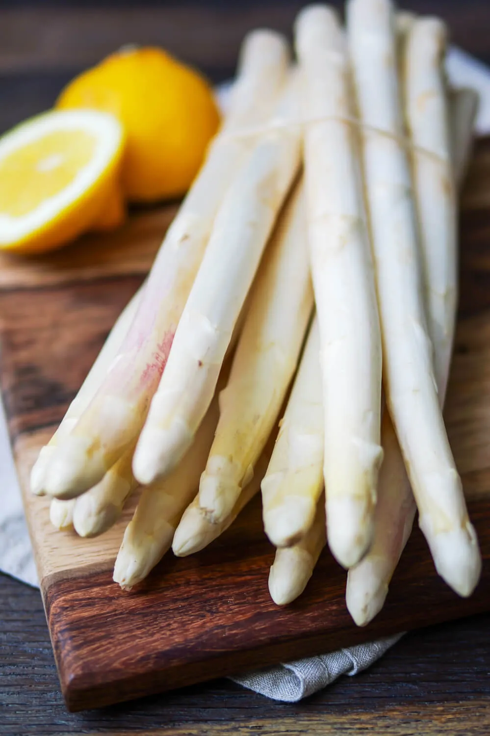 Weißer Spargel und Zitrone auf einem Holzbrett.