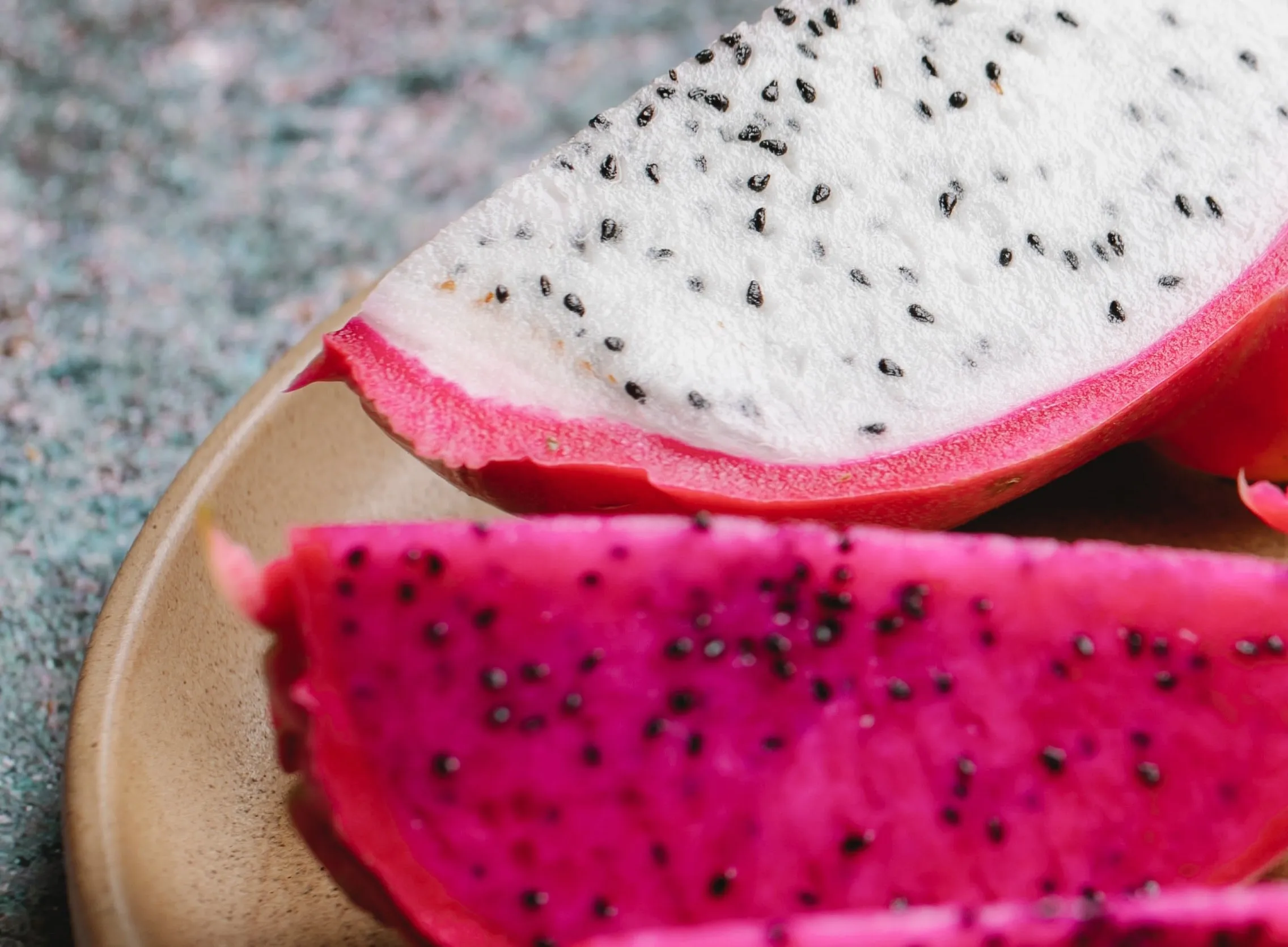 Weißes und pinkes Fruchtfleisch einer aufgeschnittenen Drachenfrucht mit schwarzen Samen auf hellem Hintergrund, das die unterschiedlichen Sorten der Drachenfrucht zeigt.