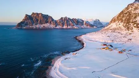 Weite und beeindruckende Landschaft der Lofoten in Norwegen, mit schroffen Bergen, tiefblauem Wasser und einem klaren Himmel.