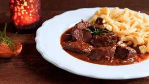 Wildgulasch mit dampfenden Spätzle und Petersilie auf einem rustikalen Teller, servierfertig.