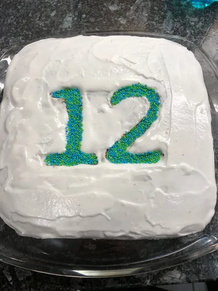 Zahlenkuchen glasieren und dekorieren: Ein gleichmäßiger weißer Zuckerguss und das vorsichtige Einfüllen von Zuckerperlen in die ausgeschnittenen Zahlen.