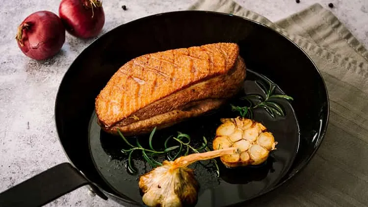 Zart rosa gebratene Entenbrust in der Pfanne mit Kräutern und Knoblauch