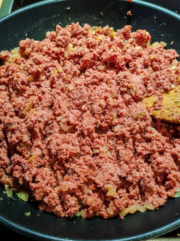 Zerdrücken und Vermengen des Corned Beefs mit Zwiebeln in der Pfanne