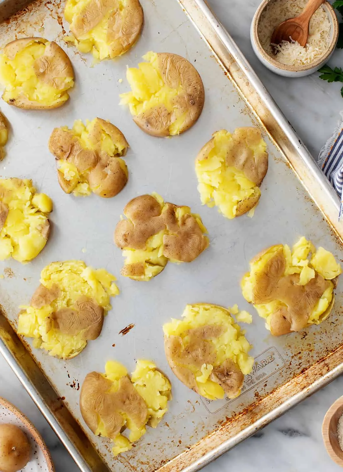 Zerdrückte Kartoffeln liegen auf einem geölten Backblech bereit zum Würzen