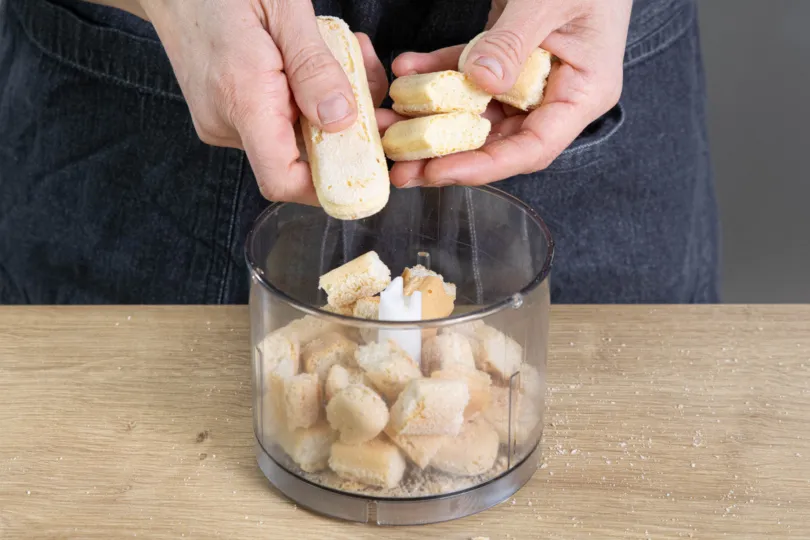 Zerkleinerter Löffelbiskuit als Basis für den Tortenboden einer Erdbeer Philadelphia Sahne Torte.