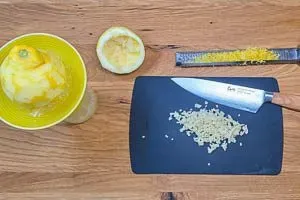 Zitrone heiß abwaschen und Schale abreiben. Knoblauchzehen in kleine Stückchen schneiden.