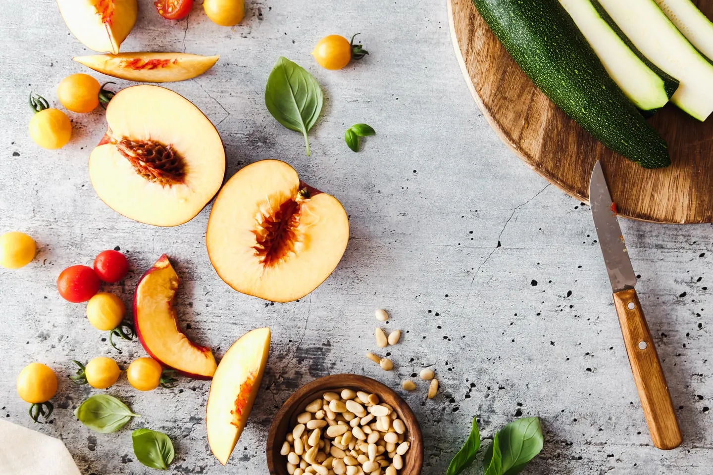 Zucchini, Pfirsiche, Pinienkerne und Tomaten auf Marmorplatte und Holzbrett