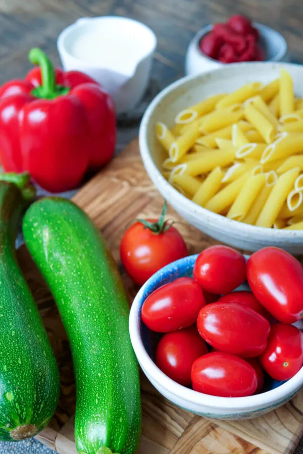 Zucchini, Tomaten, Penne, Paprika, Sahne und Tomatenmark auf dem Holzbrett